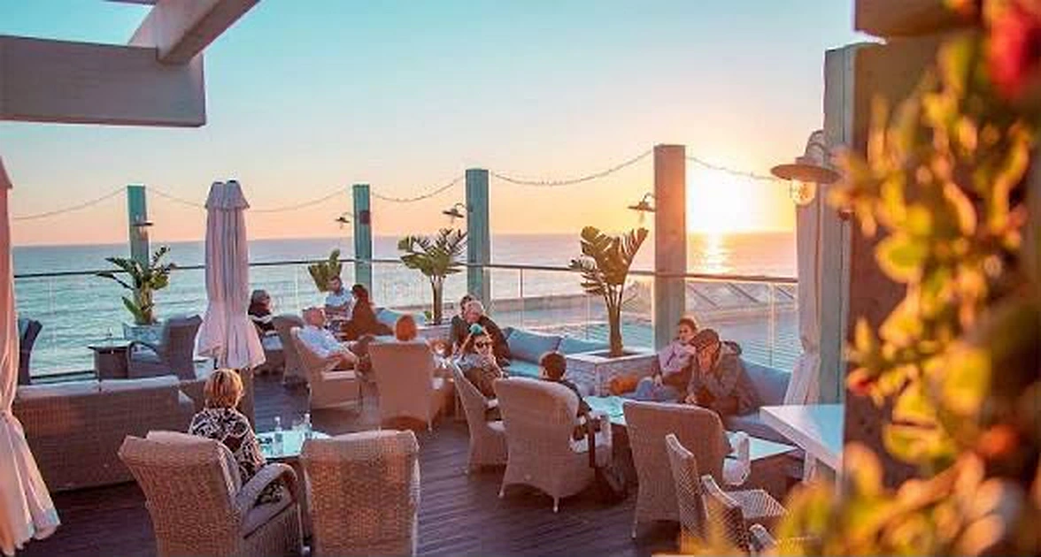 Clientes sentados numa esplanada com vista para o mar ao pôr do sol